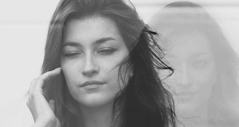 Mulher com expressão serena em foto a preto e branco com efeito de dupla exposição, sugerindo introspecção e dualidade emocional.