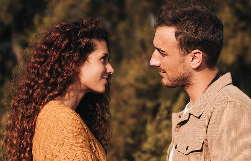 Casal feliz a olhar-se nos olhos com amor e cumplicidade, num cenário natural ao ar livre.