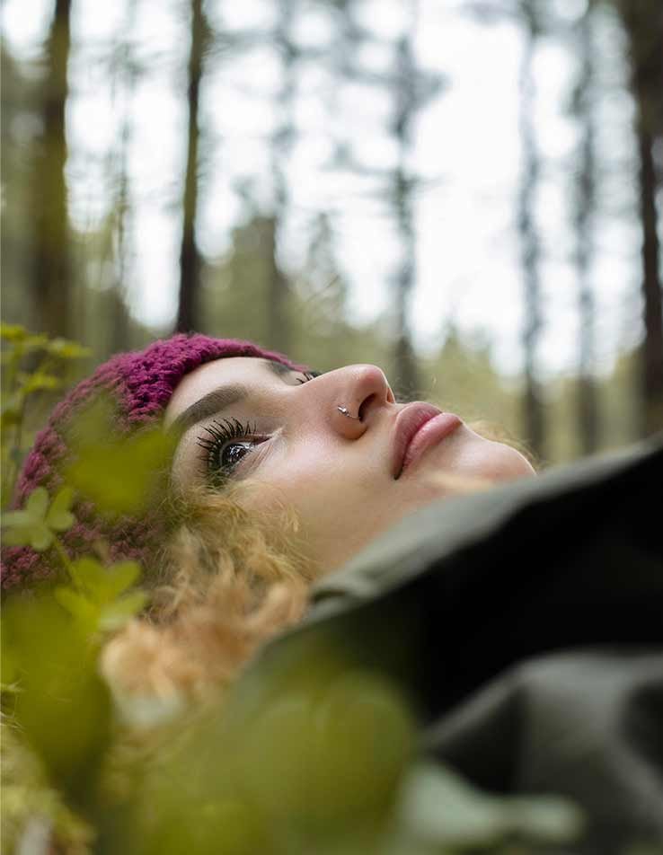 Mulher deitada na relva com expressão tranquila, olhos fechados, em momento de escuta interior e conexão com a natureza
